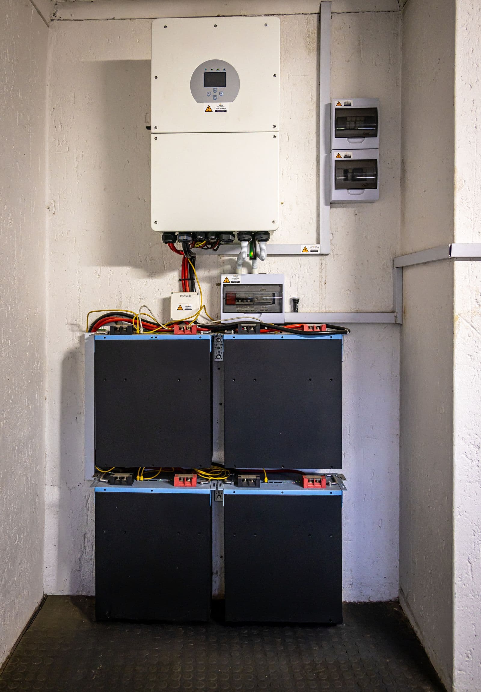 Wall-mounted inverter above a stacked home battery bank in a utility space