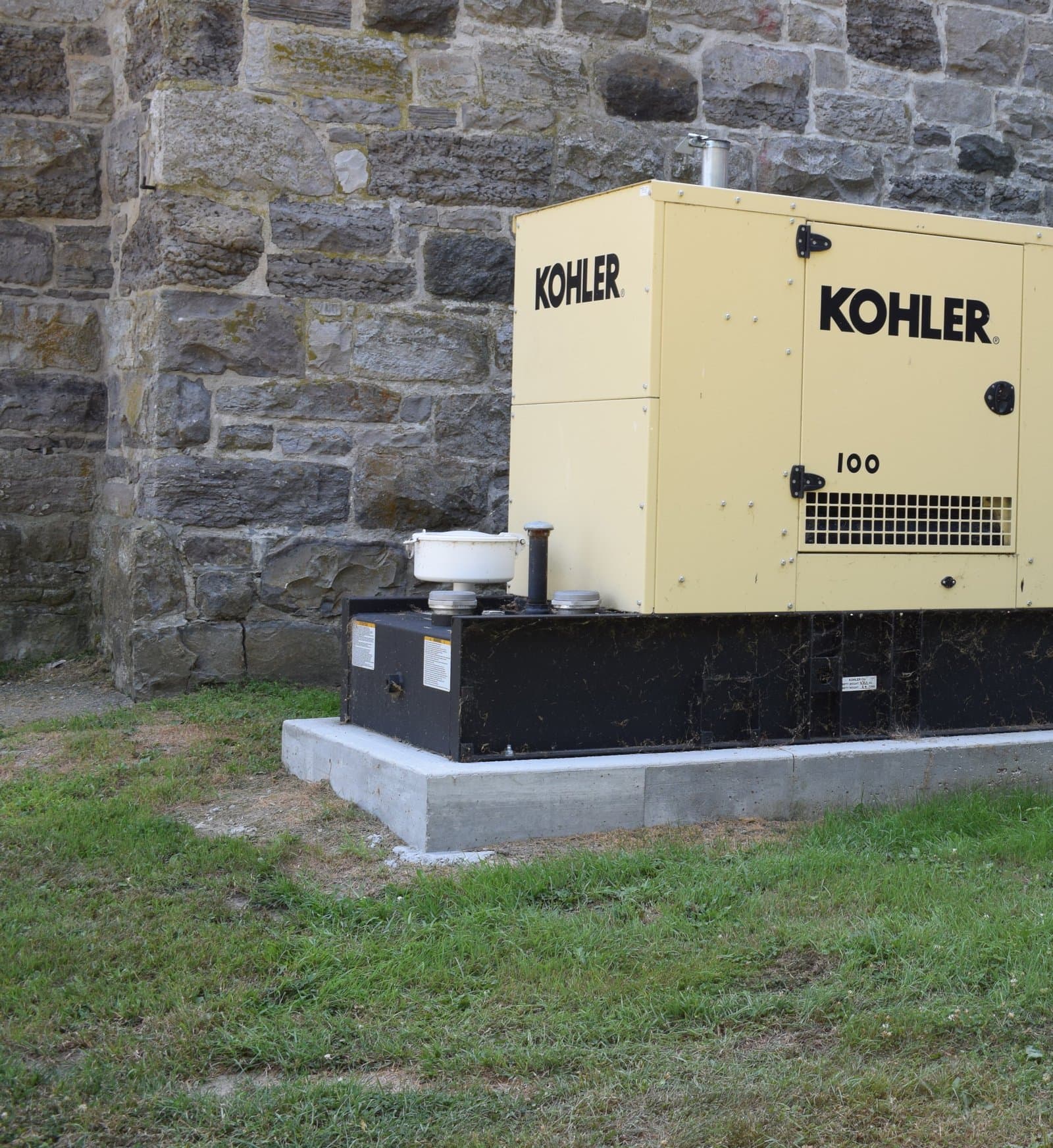 Standby generator installed on a concrete pad beside a stone building