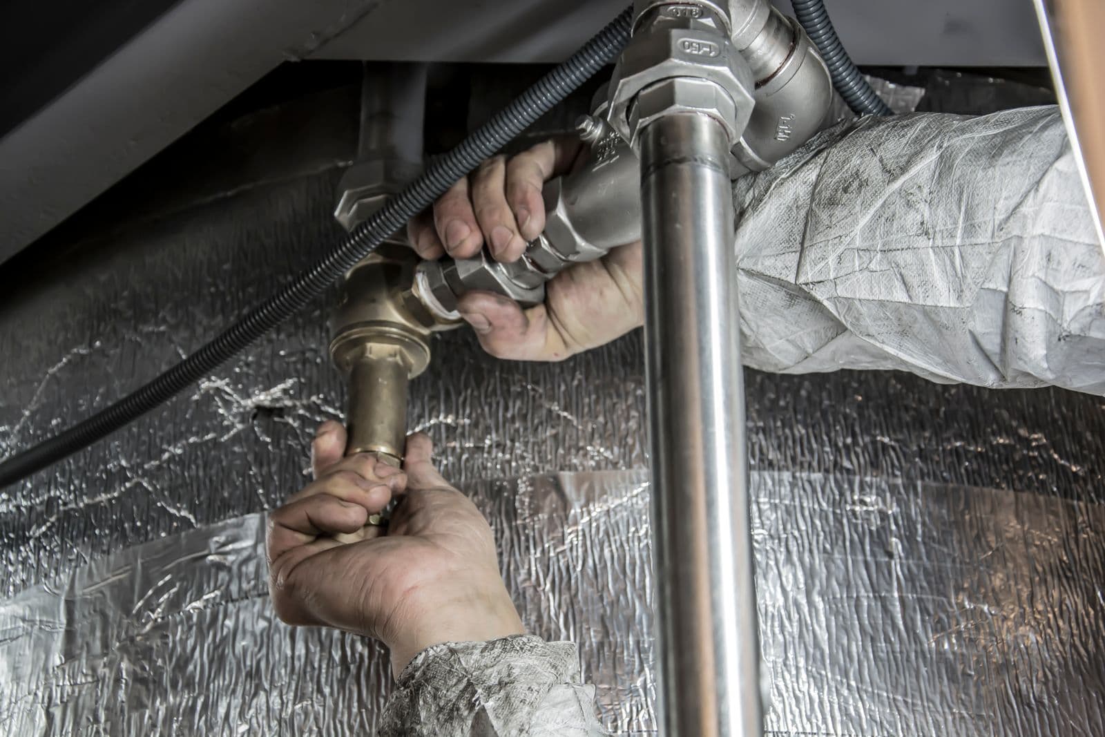 Plumber's hands tightening a threaded fitting on a water line